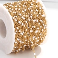 Macro shot of gold plated stainless steel cable chain with white enamel beads on a reel - Gold Chain White Beads