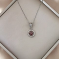 Detail showing a round ruby pendant with halo setting in a luxury jewelry box - Silver Red Zirconia