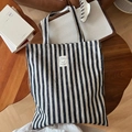 Flat lay of blue striped canvas tote bag with woven handles on a wooden table - Stripe Style