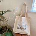Borsa tote in tela beige con ricamo Beloved blu presentata su una panca di legno - Ricamo Sfumato Blu