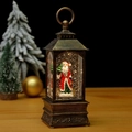Close-up of vintage bronze Christmas lantern with Santa Claus figurine and swirling glitter - Santa Carrying Tree