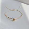 Detail eines Miyuki-Perlenarmbands mit goldenem Buchstaben H und bunten Perlen im Boho-Stil - Buchstabe H