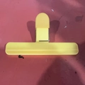 Yellow T-shaped plastic bag sealer clip with metal spring on red surface background - Beige Large