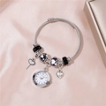 Detailed close-up of a silver beaded watch bracelet with heart and key charms on pink satin - Black