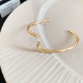 Primer plano del brazalete abierto dorado irregular sobre un plato de cerámica - Dorado - Onda Fina
