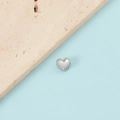 Macro shot of silver heart pendant with beaded edges on a blue and stone backdrop - Steel