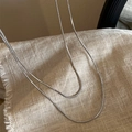 Gros plan sur la chaîne serpent argentée sur fond en lin beige de style minimaliste - Chaîne Serpent Double Couche / Argenté