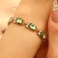 Dettaglio di bracciale dorato con pietre quadrate verde smeraldo e punti luce - Verde