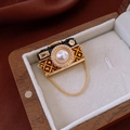 Detalle de broche de cámara vintage con esmalte negro, perla y cadena dorada colgante - Dorado