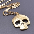 Primer plano detallado del colgante de calavera dorada con grabados florales en fondo gris - Con Collar / Dorado