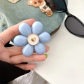 Close-up of blue flower phone socket grip with golden heart center on denim backdrop - Blue