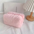 Close-up of pink plush makeup bag with fluffy texture and smooth zipper on a white desk - Pink