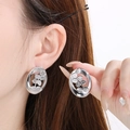 Detail shot of hollow oval leaf pattern silver earrings worn and held for scale - Silver
