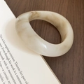 Detail of cream resin bangle with marble texture resting on an open book - Light Brown Smudge (White-Oval Concave)