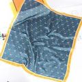 Detailed view of navy blue equestrian silk scarf with white horse pattern and orange box - Blue