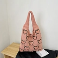 Pink knitted tote bag featuring black heart patterns on a wooden surface backdrop - Pink