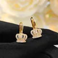 Elegant gold crown hoop earrings with sparkling cubic zirconia on black fabric background - Gold