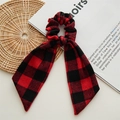 Detail van rood-zwarte geruite scrunchie met lang lint op een vintage boekachtergrond - Rode Geruite Streamer
