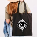 Black canvas tote bag with white graffiti evil eye print shown in a back view on a shoulder - Design F-All Seeing Eye-Black