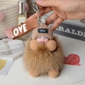 Detail of sleeping baby plush doll on fluffy brown fox fur pom pom with LOVE strap - Khaki