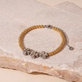 Detail van klaverbedeltjes aan een gouden roestvrijstalen armband met een stenen achtergrond - Gouden Kralen Klaver Stijl