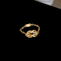 Detail eines goldenen Kettenrings mit zirkoniabesetztem Hufeisenknoten und Metallplakette - Gold