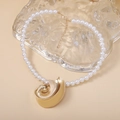 Primer plano de un collar de perlas blancas con un gran colgante dorado en forma de concha - Collar C-Perla con Colgante Grande