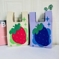 Detail of knitted tote bags featuring red strawberry and blue berry patterns on soft yarn - Strawberry Purple