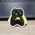 Cute black cat acrylic pin wearing a yellow cloak with a rainbow star pattern - Cape Black Cat