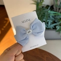 Close-up of light blue linen bow hair clip with white resin heart on display card - Blue Bowknot Duckbill Clip