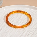 Primer plano de un brazalete de resina ámbar con patrón de carey en bandeja blanca - Estilo de Borde Delgado con Textura de Carey Café