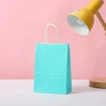 Cyan kraft paper gift bag with white twisted handles on a desk next to a lamp - 15*11*6 / Sky Blue