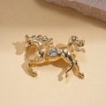 Dettaglio macro di una spilla a cavallo dorata con cristallo rotondo su pietra beige liscia - Stile Cavallo in Corsa con Strass / Oro-Bianco