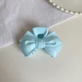 Detailed top view of a light blue cream-colored double bow hair claw clip on a textured surface - 9cm / Glossy Blue Bow