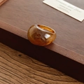 Vista dettagliata di un anello ovale in resina ambrata su un vassoio di legno rustico - Tartarugato ambra / Caffè Scuro