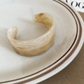 Detailed view of wide cream marble acrylic cuff bracelet with wavy edges on ceramic plate - Light Coffee