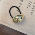 Dettaglio dell'elastico nero con elemento metallico dorato lucido a forma di fagiolo - Stile Largo Oro