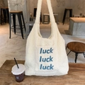 Detailaufnahme der cremefarbenen Fleece-Tasche mit blauer Luck-Stickerei im Café - Triple Luck Buchstabenstickerei / Triple Luck / Weiß