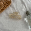 Detail of medium marble-textured hair claw clip on white fabric with lifestyle decor - Medium Square Claw / Beige