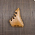 Macro shot of sandalwood scalp massage comb with five polished teeth on bamboo mat - Golden Sandalwood Small Monster Shape (11.5*7.5*2cm)