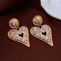 Vista macro de pendientes de corazón dorados martillados con detalles de strass cristal - Estilo Corazón Dorado