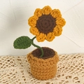 Handgehäkeltes Sonnenblumen-Topfornament auf beigefarbener Spitze mit grünen Blättern - Sonnenblume / Gelb