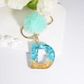 Letter D resin keychain with blue stones, gold foil, and a mint green pompom - Letter D
