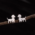 Minimalist silver stainless steel dachshund stud earrings displayed on a dark wooden branch - Sitting Dachshund (780) / Steel