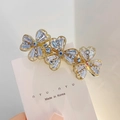 Pince à cheveux trèfle doré avec zircons bleus et clairs sur support minimaliste - Style Fleur à Trois Pétales