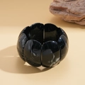 Makroaufnahme eines klobigen Marmorharz-Armbands mit geometrischen Segmenten auf Stein - Schwarzes Armband Mit Marmortextur In Blütenblattform