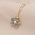 Collana dorata con pendente a fiore blu e perle su uno sfondo di tessuto morbido - Blu