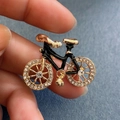 Spilla bici dorata con smalto nero e strass bianchi su un tessuto blu scuro ruvido - Piccola Bicicletta Nera