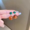 Macro detail of vintage resin earrings in dark green and amber with gold accents - Brown Square