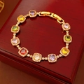Detailed close-up of vintage gold bracelet with colorful square zircons on wood box - Gold-Multicolor